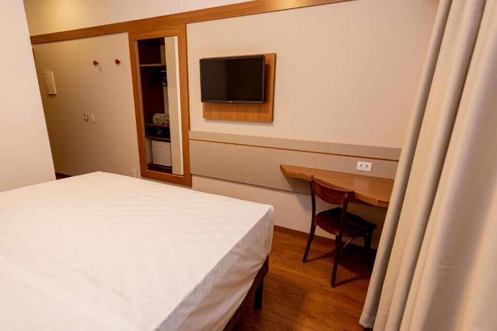 Habitación de hotel con cama, escritorio y televisor montado en la pared.