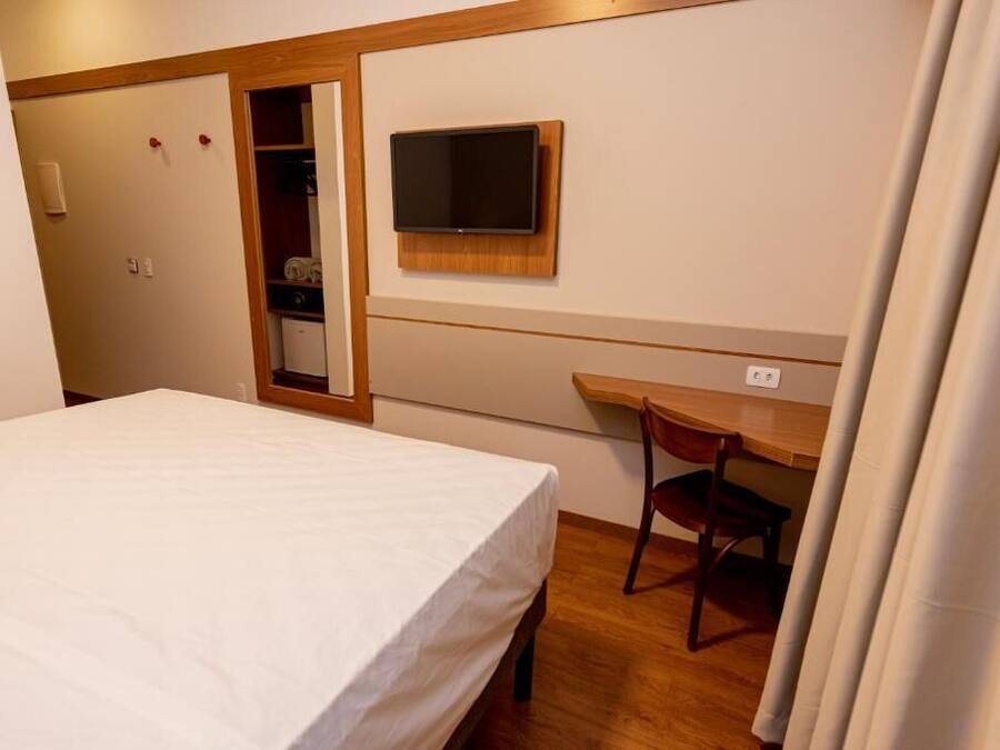 Habitación de hotel con cama, escritorio y televisor montado en la pared.