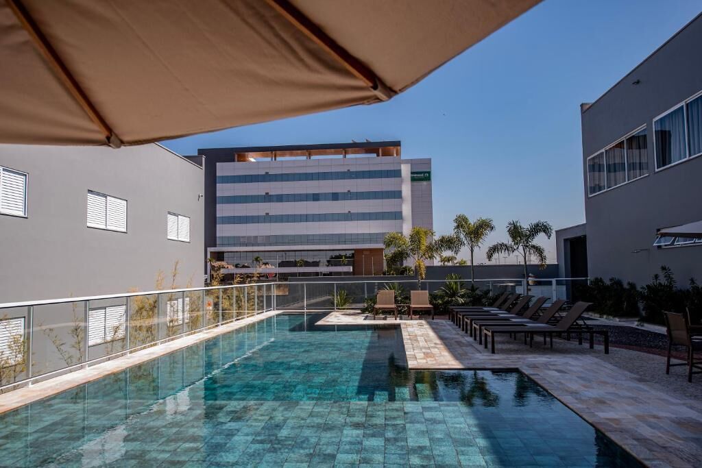 A swimming pool with lounge chairs and umbrellas, surrounded by buildings.