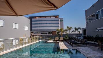 A swimming pool with lounge chairs and umbrellas, surrounded by buildings.