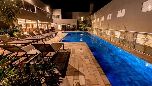 Zona de piscina iluminada por la noche con sillones de descanso y un bar.