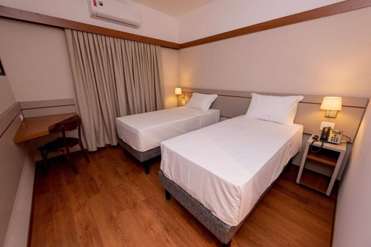 Habitación de hotel con dos camas individuales, un escritorio, una silla, un teléfono y una cortina.