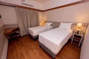 Una habitación de hotel con dos camas individuales, un escritorio, una silla, un teléfono y una cortina.