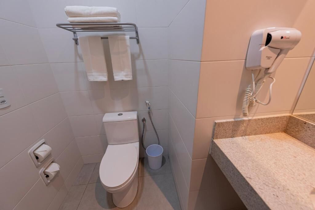 Een badkamer met een toilet, een handdoekhouder, een haardroger en een prullenbak.