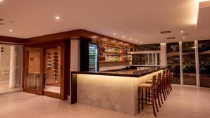 Un área de bar moderna con mostrador de mármol, taburetes y una estantería llena de licores.
