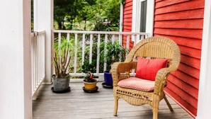 A wicker chair with a red cushion on a wooden porch with potted plants.