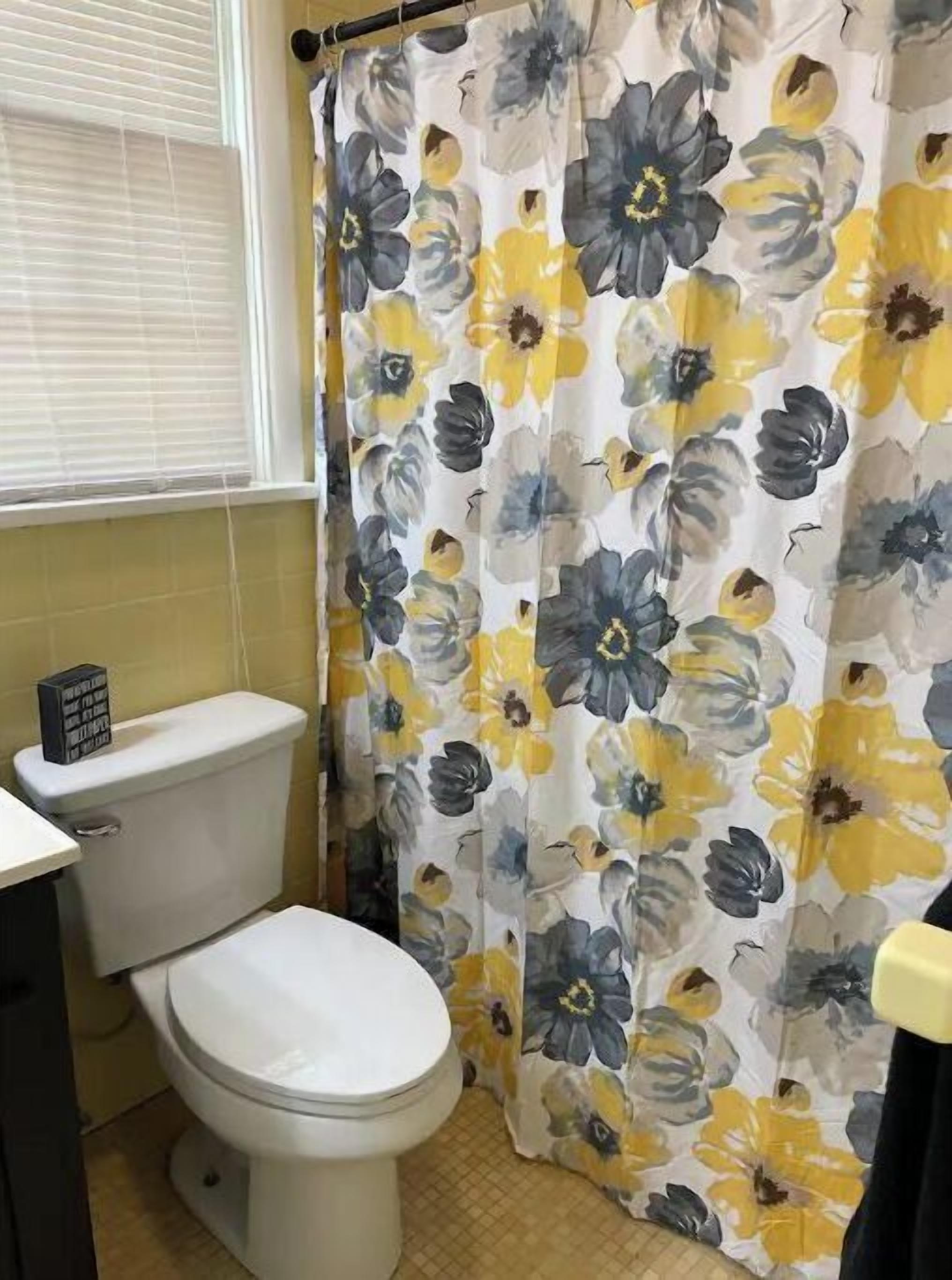 Un baño con inodoro, lavamanos y cortina de ducha estampada con motivos florales.