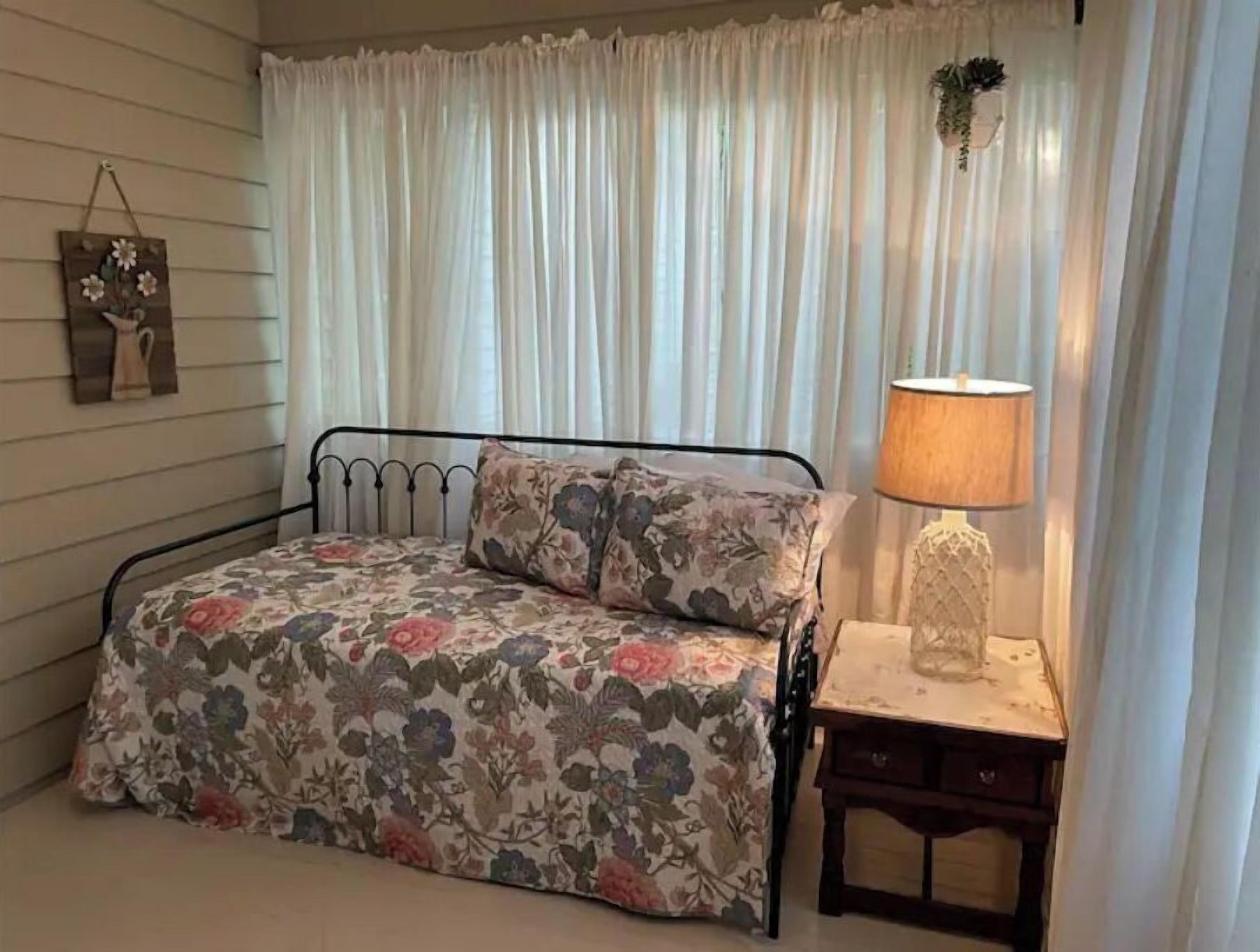 Een slaapkamer met een bed, nachtkastje, lamp en raam met gordijnen.