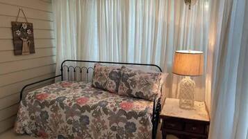 Een slaapkamer met een bed, nachtkastje, lamp en raam met gordijnen.