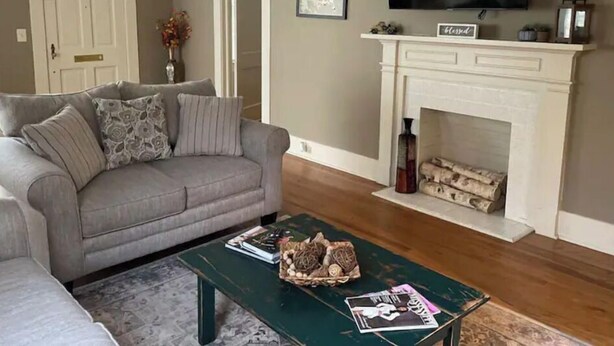 Un salon avec un canapé gris, une table basse verte, une cheminée et un téléviseur à écran plat fixé au mur.