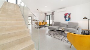 A modern living room with a staircase, a dining area, and a large window.