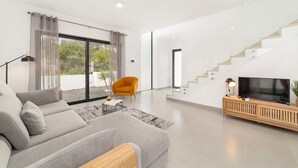 A modern living room with a sofa, a TV on a wooden console, a staircase, and a large window with curtains.