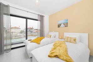 A hotel room with two beds, a large window, and a painting on the wall.