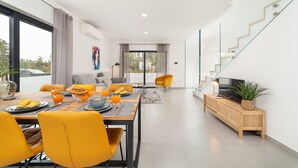 A modern living space with a dining area, sofa, TV, and staircase.