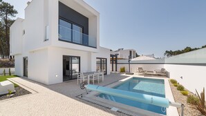 A modern two-story house with a swimming pool, outdoor seating, and a clear sky.