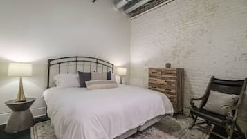 Ein Schlafzimmer mit einem Bett, Nachttischlampen, einem Schminktisch und einem Sessel.