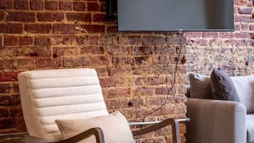 Ein modernes Wohnzimmer mit Backsteinwand, einem Wand-Fernseher, einem weißen Sessel und einem grauen Sofa.