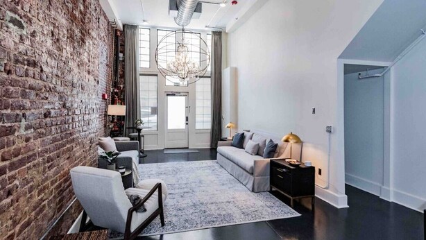 A modern living room with a brick wall, a sofa, a coffee table, and a chandelier. - Fabulous Loft w/ King Suite Great Location! (Birmingham)