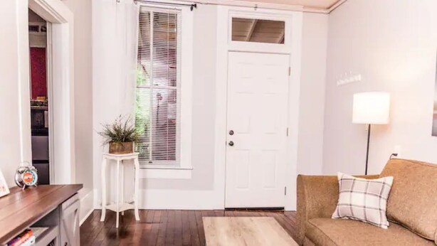Una sala de estar con una puerta blanca, un sofá marrón, una mesita y una lámpara.