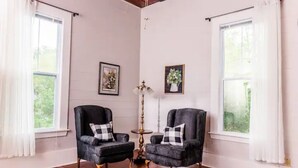 Una habitación con dos sillones negros, una mesita redonda y una lámpara de pie. Hay dos cuadros en la pared.