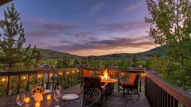 A wooden deck with a table set for dining, a fire pit, and string lights.