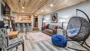A cozy living room with a wooden ceiling, a hanging chair, a sofa, and a coffee table.