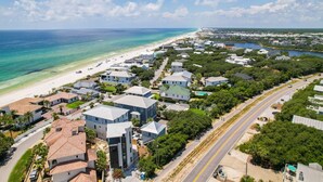 An aerial view of a coastal residential area with houses, a beach, and a road.