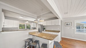 A kitchen with white cabinets, a granite countertop, and three bar stools.