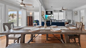 A dining area with a wooden table set for six, a vase with flowers, and a TV in the background.