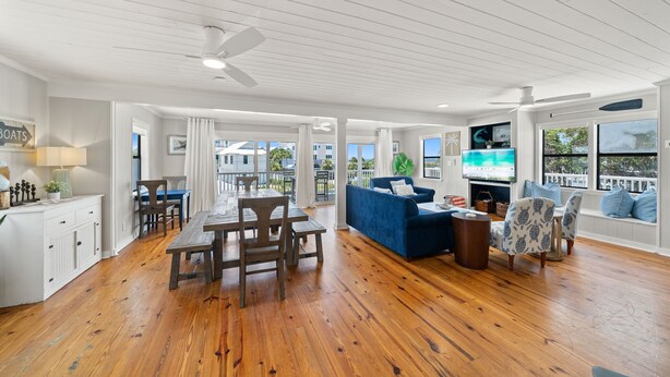 A spacious living area with a wooden floor, a dining table with chairs, a blue sofa, and a TV.