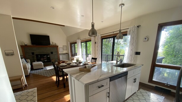 A modern kitchen with a large island, wooden flooring, and a dining area with a fireplace. - Modern open concept house w/Lake George views, private beach- 5 mins to village  (Lake George)