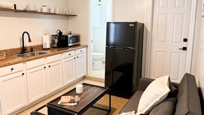 A compact living space with a kitchenette, a black refrigerator, a dark sofa with a white throw, and a small coffee table.