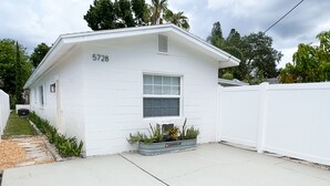 A white single-story house with the number 5728 on the front wall, a small front yard with a concrete path, and a white fence surrounding the property.