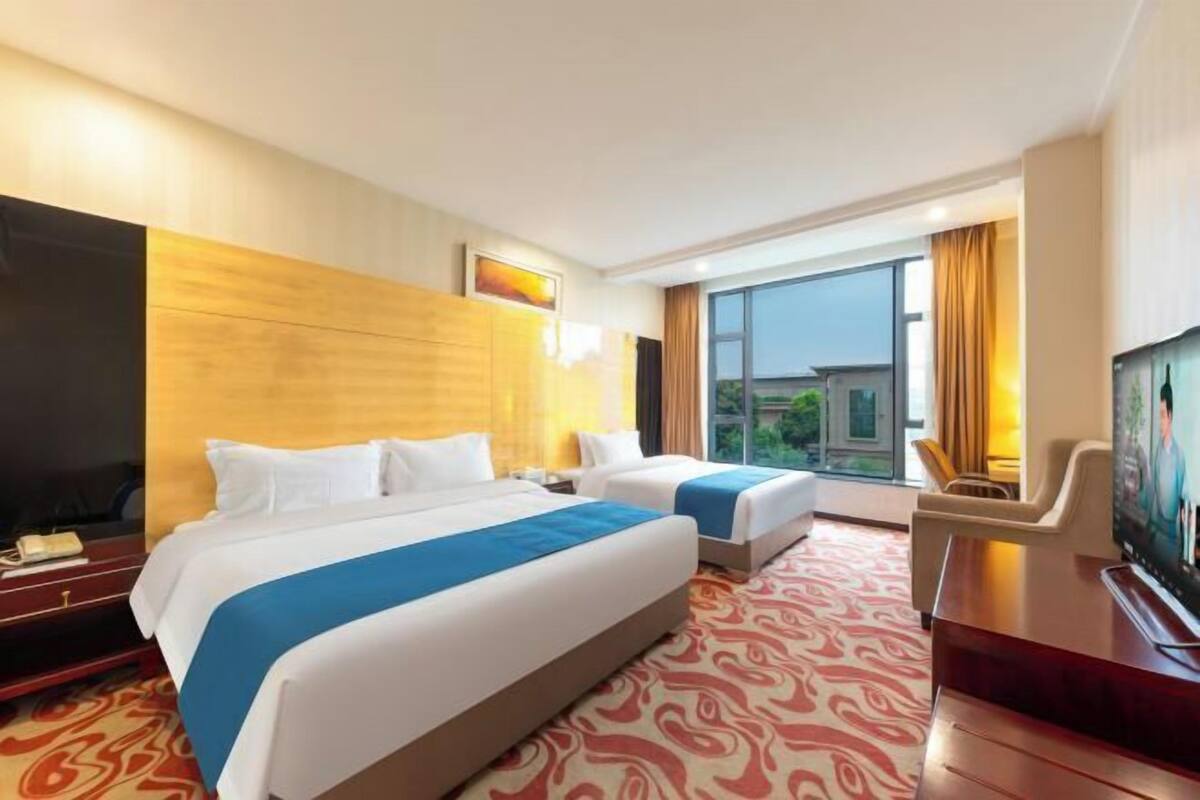 A hotel room with two beds, a TV, a desk, and a large window.