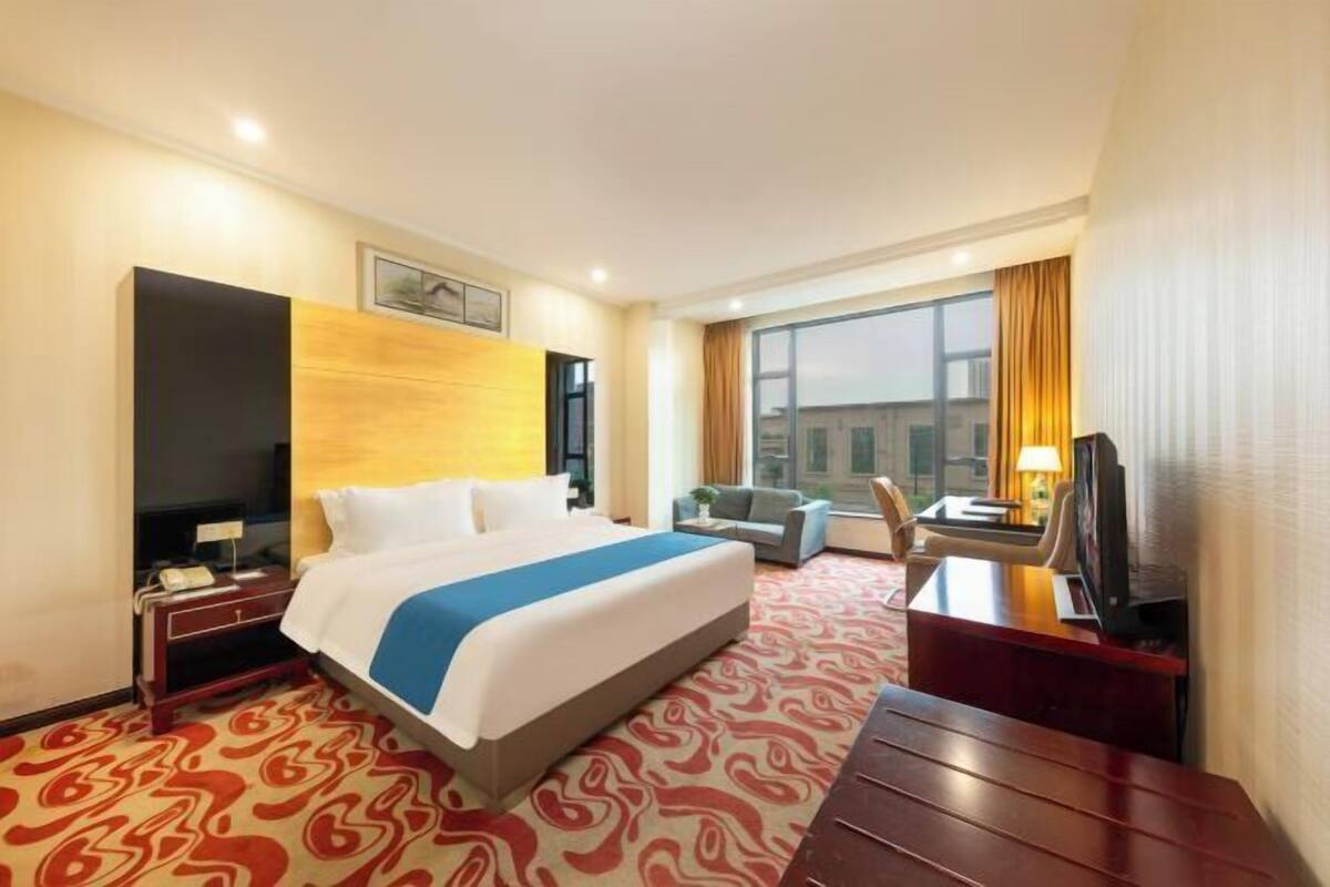 A hotel room with a bed, a desk, a chair, a TV, and a window with curtains.