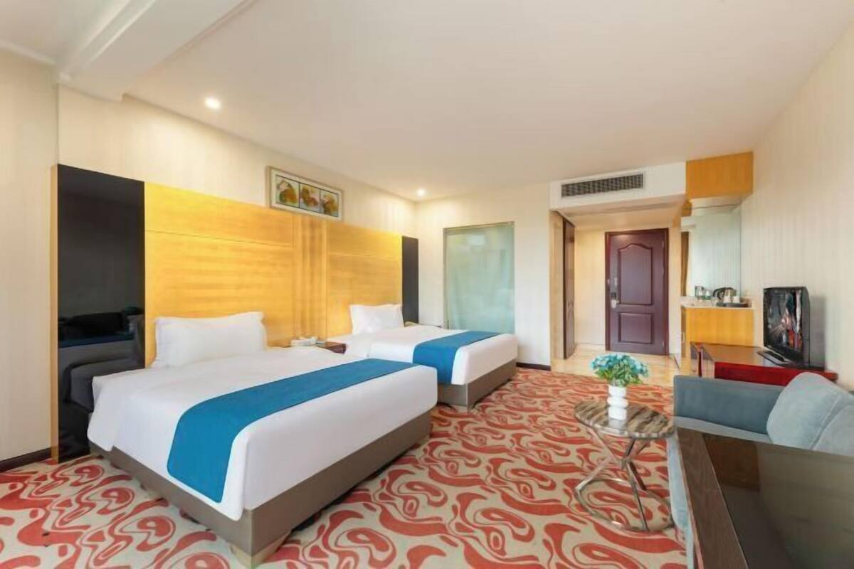 A hotel room with two beds, a television, a small table with a plant, and a sofa.