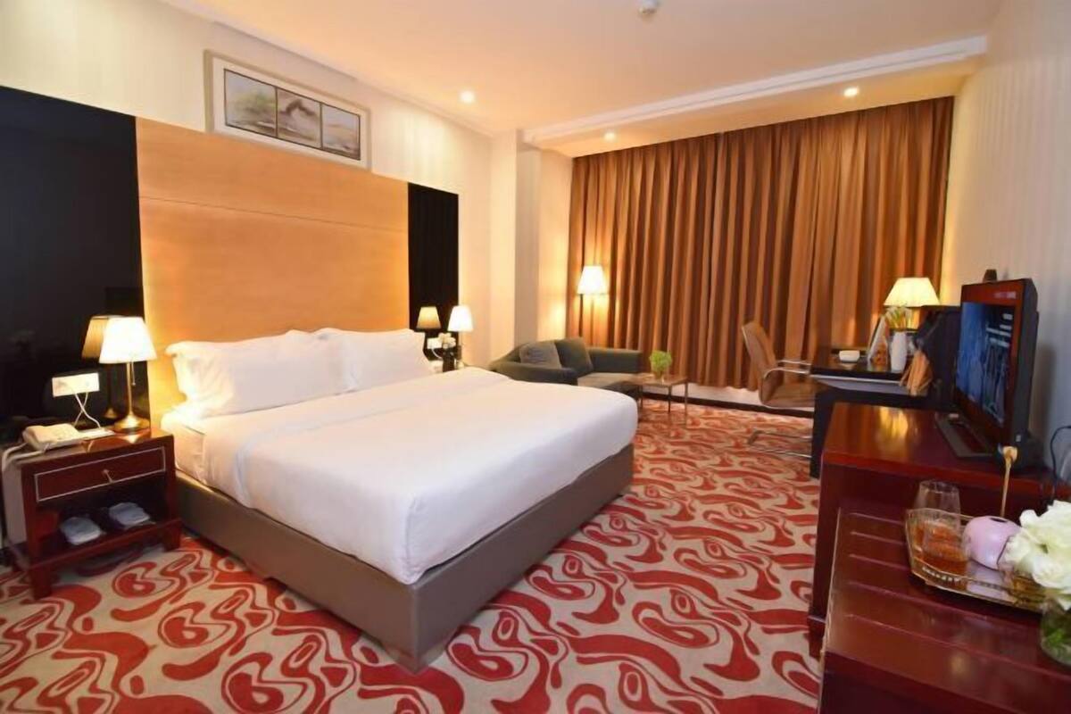 A hotel room with a large bed, a desk with a TV, a chair, and a desk lamp.