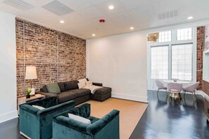 A modern living room with a brick wall, a sectional sofa, a round table with chairs, and large windows.