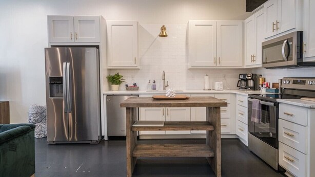 A modern kitchen with white cabinetry, stainless steel appliances, and a wooden table. - Incredible Loft w/ King Bed and Best Location (Birmingham)