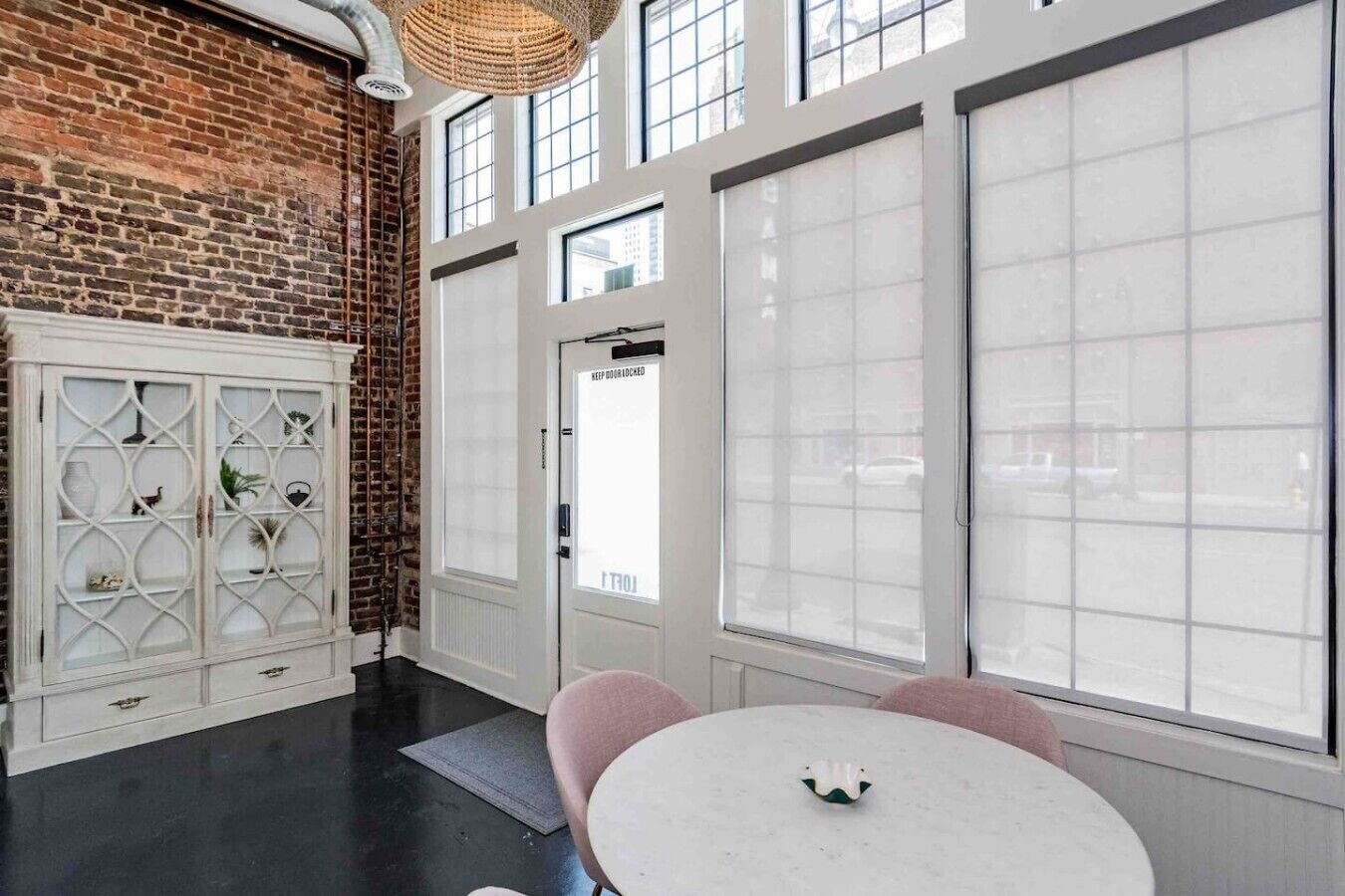 A room with a brick wall, large windows, a white cabinet, and a round table.