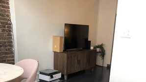 A modern living room with a flat-screen TV, a wooden cabinet, a round table with chairs, and a potted plant. - Incredible Loft w/ King Bed and Best Location (Birmingham)