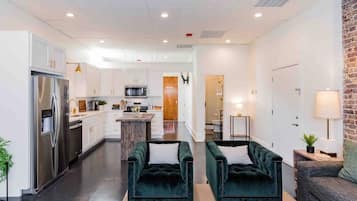 A modern kitchen with white cabinets and stainless steel appliances, a central island, and a cozy seating area with green upholstered chairs.