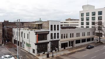 A street view with buildings, including a white building with a green sign, a parking lot, and a clear sky.