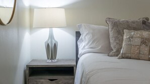 A neatly made bed with white bedding and two decorative pillows, a modern floor lamp, and a small wooden nightstand. - Incredible Loft w/ King Bed and Best Location (Birmingham)