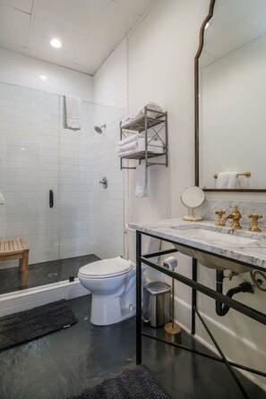 Un bagno moderno con un water bianco, una doccia, un lavabo in marmo con accessori dorati e un porta asciugamani.