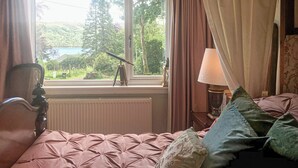 A bedroom with a bed, a window with curtains, a lamp, and a telescope on a windowsill.