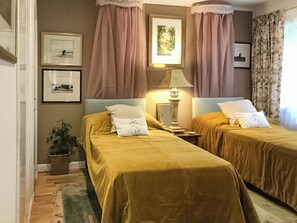 Una habitación de hotel con dos camas, una mesita de noche, una lámpara y cuadros en la pared.