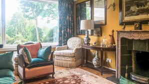 A cozy room with a large window, a fireplace, a chair, and a table with a lamp.