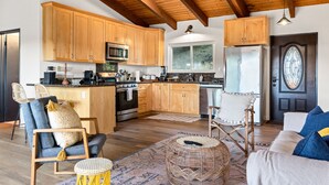 A spacious kitchen with wooden cabinets, a microwave, and a refrigerator. There are two chairs and a small round table in the living area.