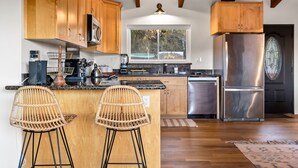 A kitchen with wooden cabinets, a stainless steel refrigerator, a large window, and a bar area with two wicker chairs.